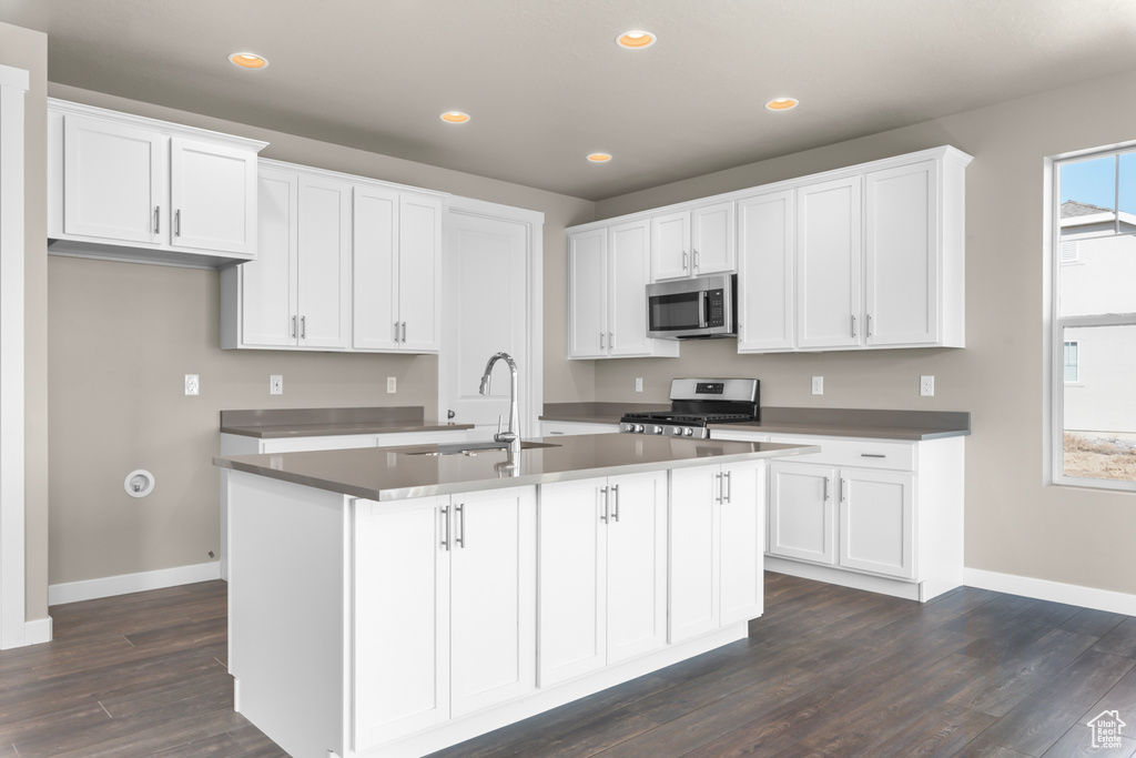 Kitchen with a kitchen island with sink, white cabinets, dark hardwood / wood-style floors, appliances with stainless steel finishes, and sink