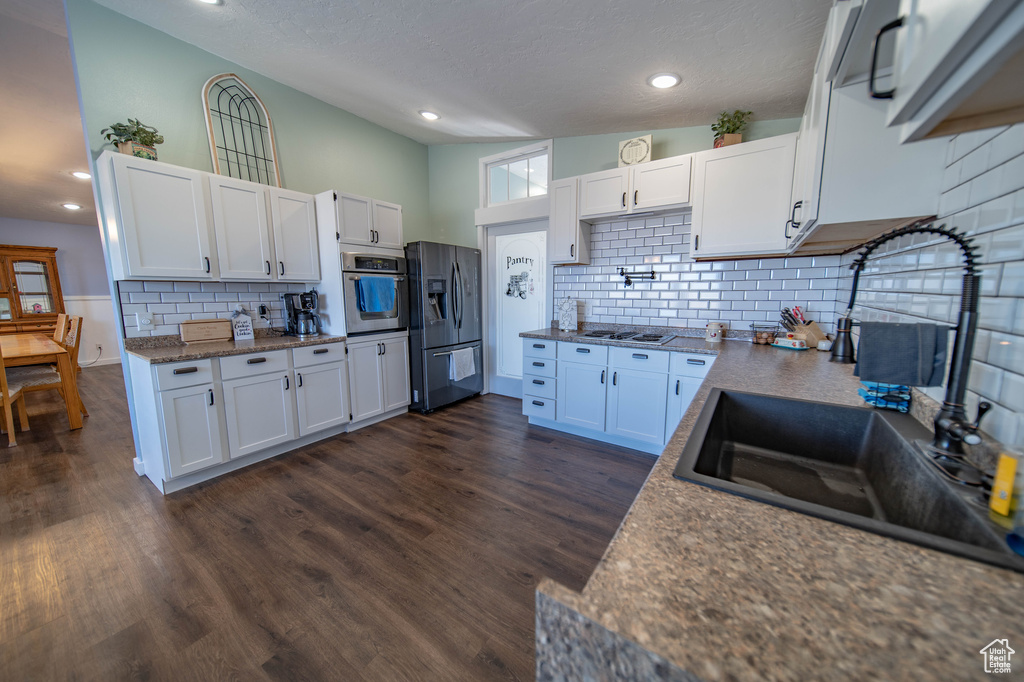 Kitchen featuring backsplash, white cabinetry, stainless steel appliances, and dark wood-type flooring