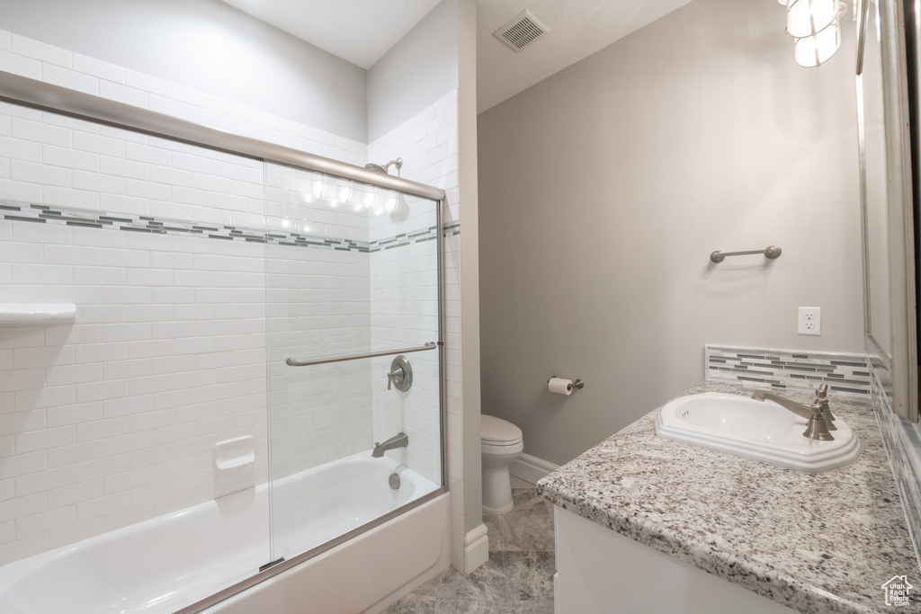 Full bathroom with tile floors, toilet, shower / bath combination with glass door, and vanity