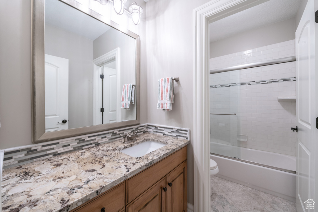 Full bathroom featuring large vanity, backsplash, enclosed tub / shower combo, tile flooring, and toilet