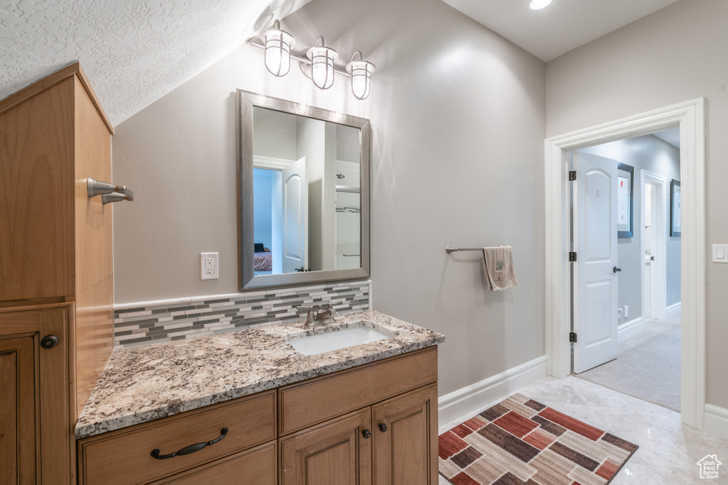 Bathroom with tile flooring, vanity with extensive cabinet space, a textured ceiling, backsplash, and vaulted ceiling