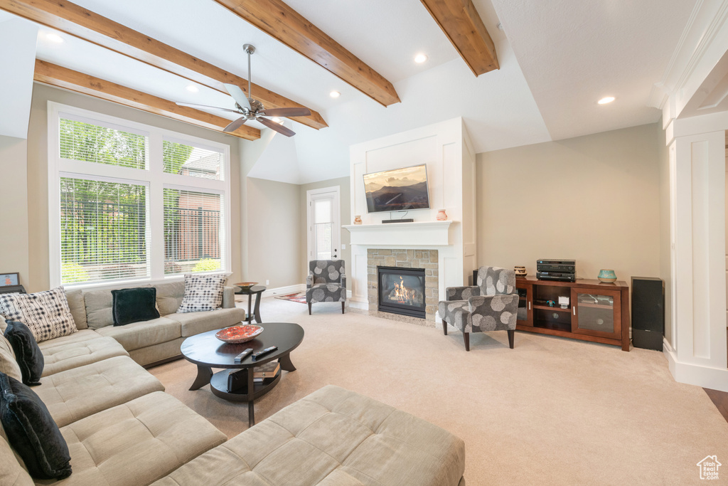 Carpeted living room featuring a stone fireplace, beam ceiling, and ceiling fan