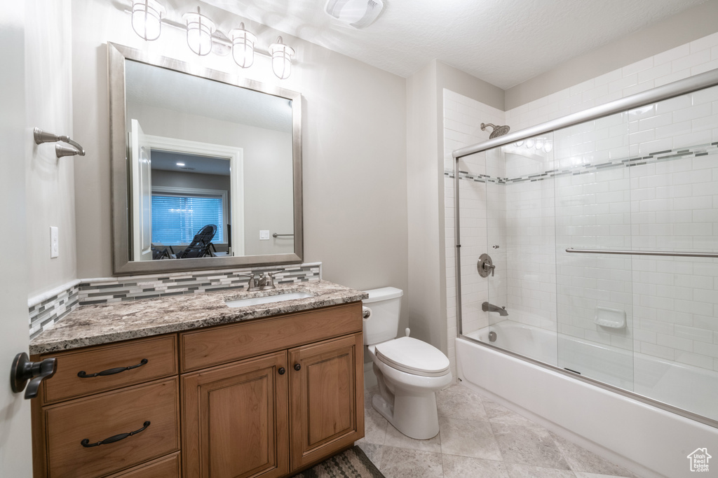 Full bathroom featuring tile flooring, vanity with extensive cabinet space, backsplash, toilet, and shower / bath combination with glass door