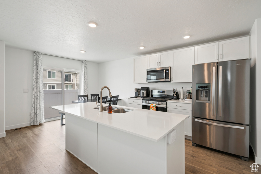 Kitchen featuring sink, appliances with stainless steel finishes, white cabinetry, and a kitchen island with sink