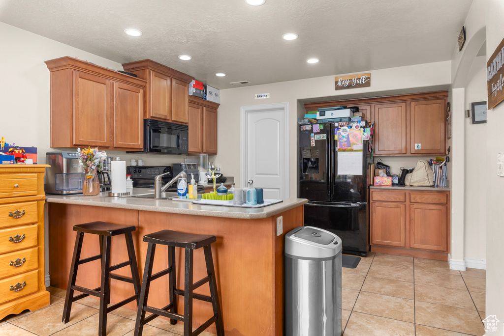 Kitchen featuring a kitchen bar, kitchen peninsula, light tile floors, and black appliances