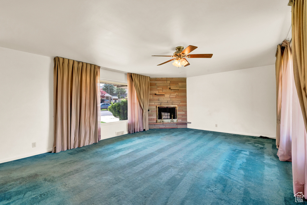 Unfurnished living room with ceiling fan, dark carpet, and a stone fireplace
