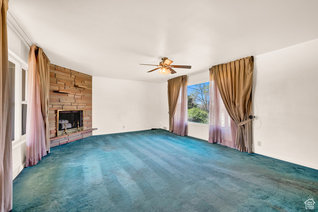 Unfurnished living room featuring dark colored carpet, ceiling fan, and a fireplace