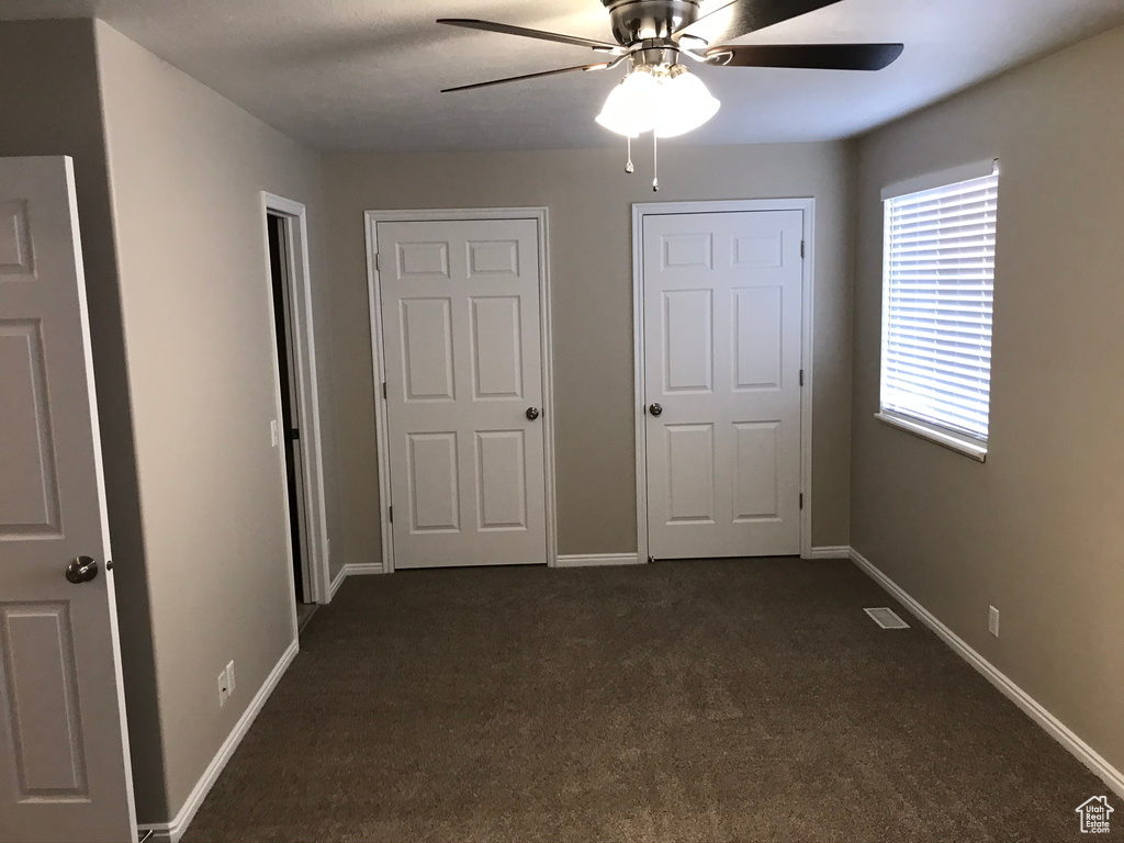 Unfurnished bedroom featuring dark colored carpet and ceiling fan