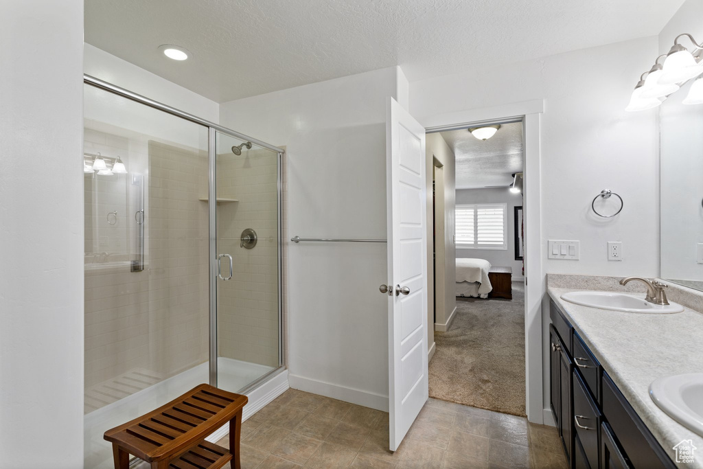 Bathroom with a shower with shower door, double vanity, tile flooring, and a textured ceiling