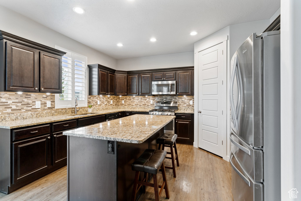 Kitchen with appliances with stainless steel finishes, backsplash, a kitchen island, and light wood-type flooring