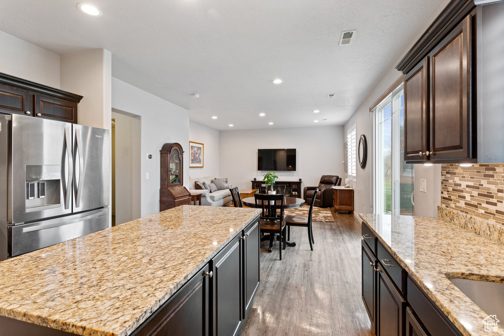 Kitchen featuring backsplash, a kitchen island, stainless steel refrigerator with ice dispenser, a healthy amount of sunlight, and light wood-type flooring