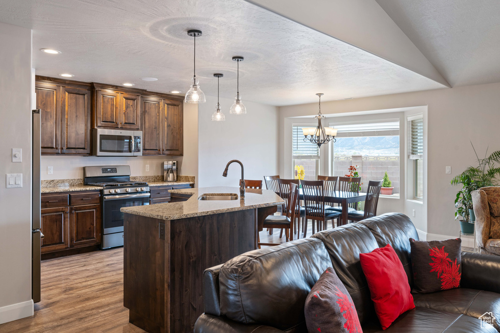 Kitchen featuring appliances with stainless steel finishes, a center island with sink, sink, a notable chandelier, and light hardwood / wood-style floors