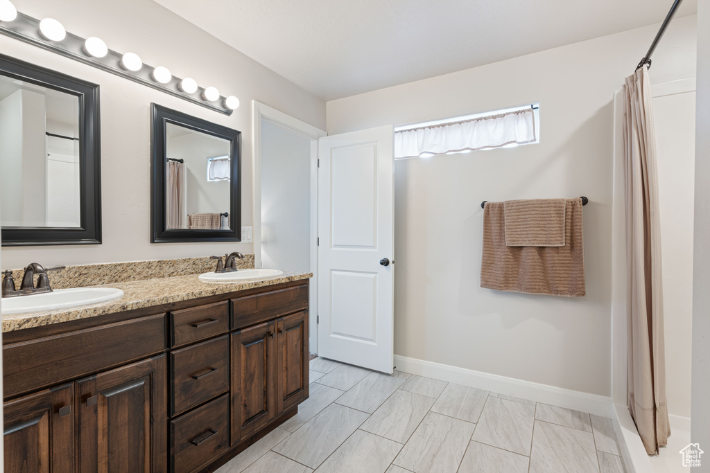 Bathroom with tile floors, vanity with extensive cabinet space, and double sink