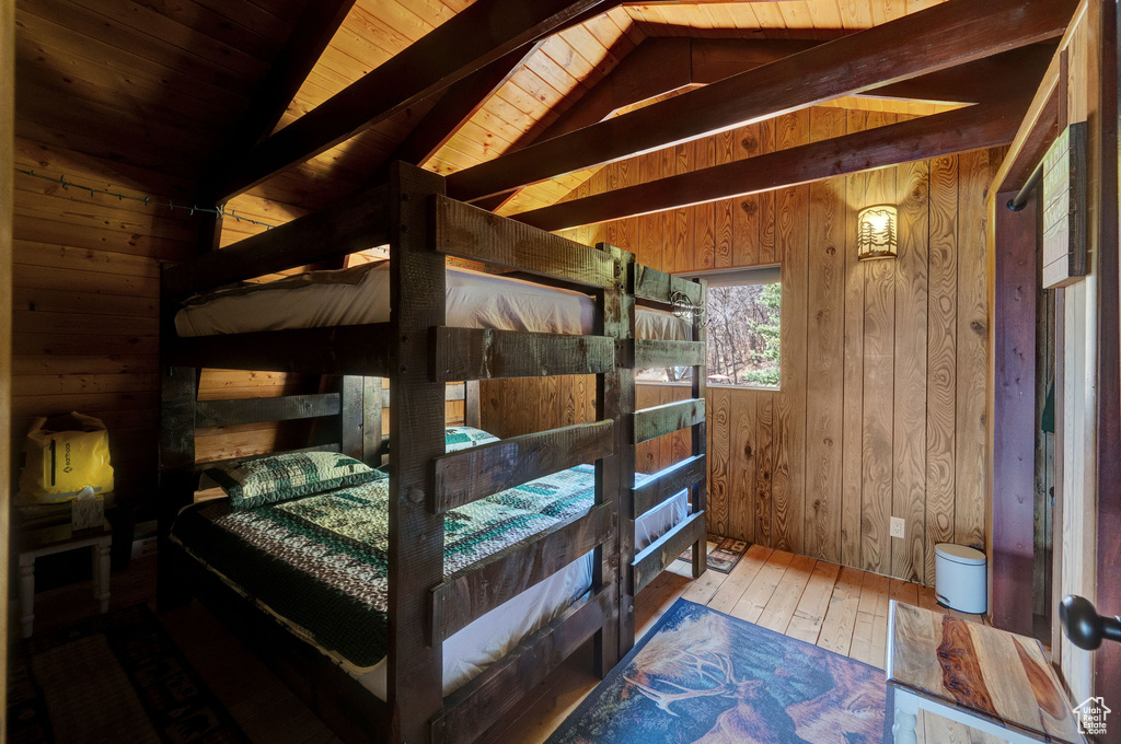 Bedroom with wood ceiling, vaulted ceiling with beams, hardwood / wood-style flooring, and wooden walls