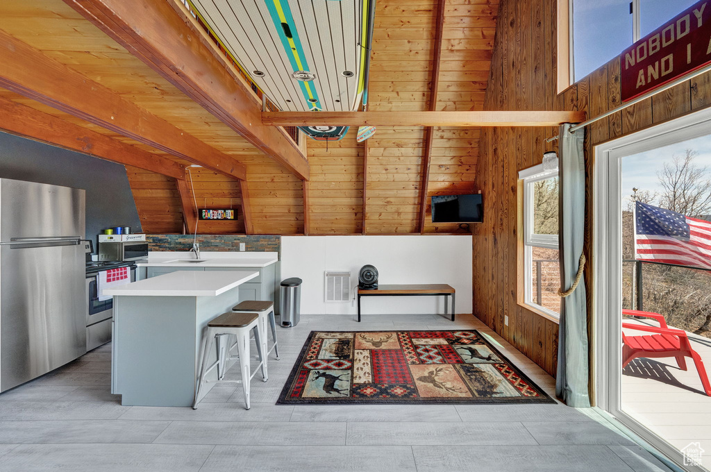 Kitchen featuring beamed ceiling, a breakfast bar, stainless steel refrigerator, wooden ceiling, and wood walls