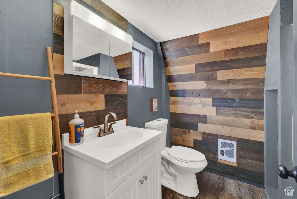 Bathroom featuring a textured ceiling, oversized vanity, toilet, wood walls, and hardwood / wood-style flooring