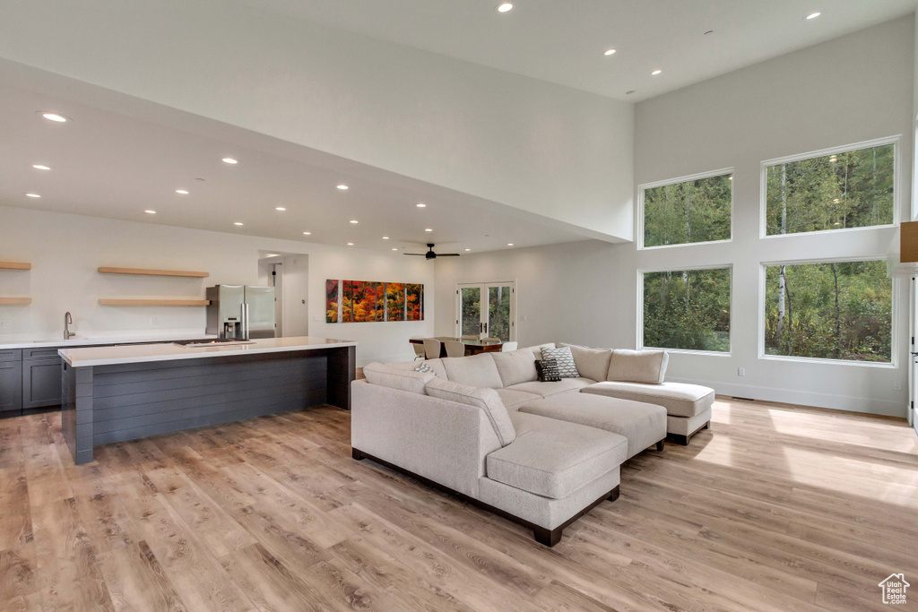 Living room with a wealth of natural light, a towering ceiling, light hardwood / wood-style flooring, and ceiling fan