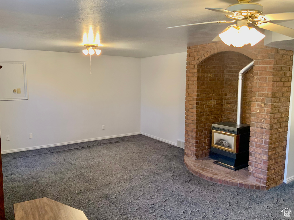 Unfurnished living room with brick wall, ceiling fan, a wood stove, and dark colored carpet
