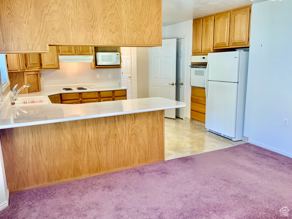 Kitchen with kitchen peninsula, light colored carpet, white appliances, and sink