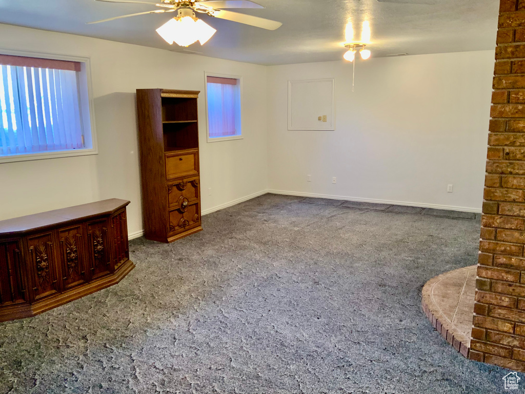Carpeted spare room featuring brick wall and ceiling fan