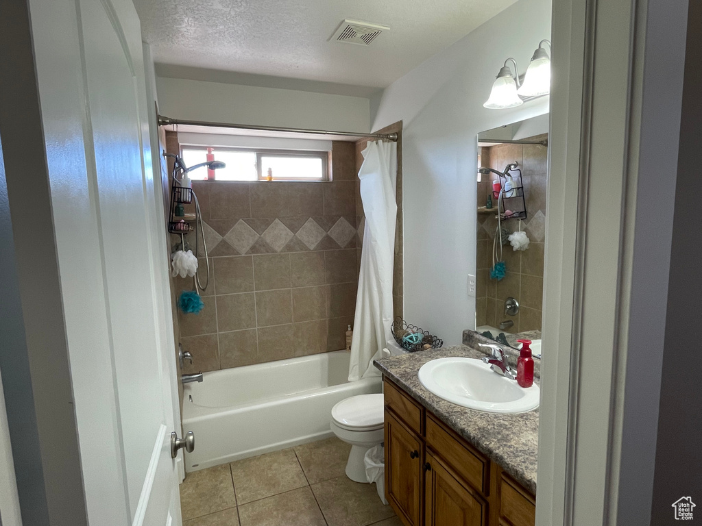Full bathroom featuring shower / bath combo with shower curtain, a textured ceiling, tile floors, toilet, and vanity