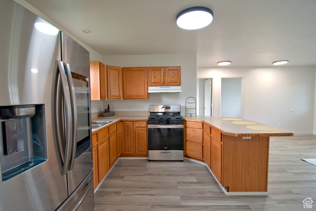 Kitchen featuring kitchen peninsula, a kitchen bar, stainless steel appliances, sink, and light wood-type flooring