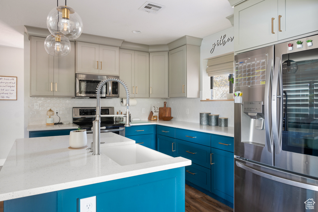 Kitchen featuring decorative light fixtures, appliances with stainless steel finishes, dark wood-type flooring, an island with sink, and blue cabinets