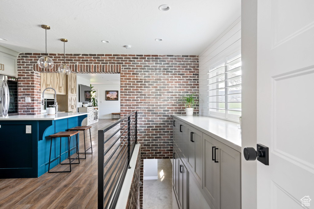 Kitchen with a breakfast bar area, hardwood / wood-style flooring, pendant lighting, and brick wall