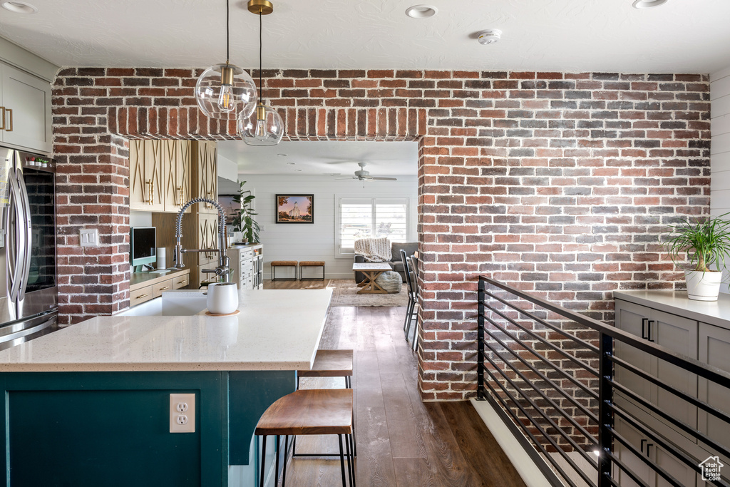 Kitchen with pendant lighting, dark hardwood / wood-style floors, brick wall, stainless steel fridge, and ceiling fan