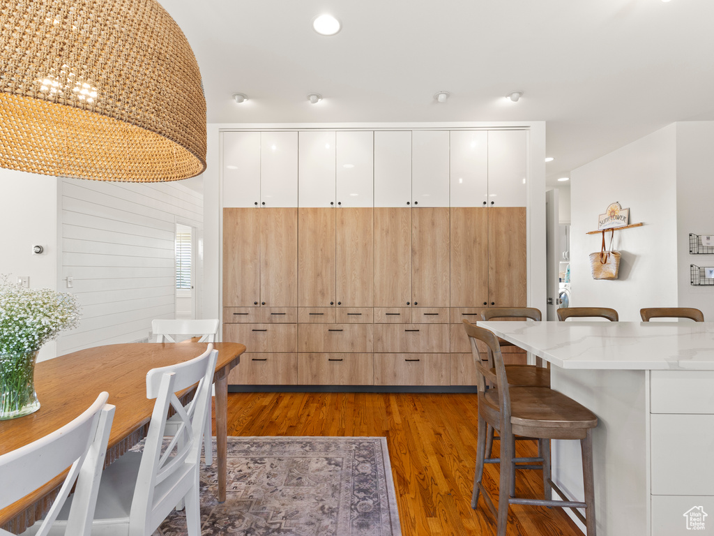 Kitchen featuring white cabinets, hardwood / wood-style floors, a breakfast bar, and light stone countertops