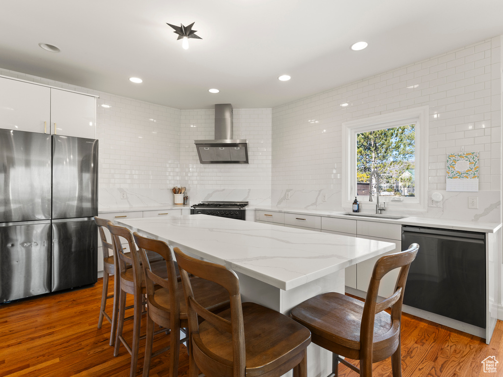 Interior space featuring sink, wall chimney range hood, light wood-type flooring, tasteful backsplash, and stainless steel appliances