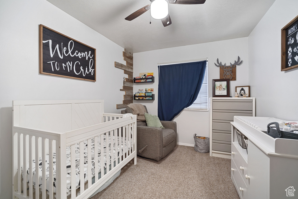 Bedroom featuring light carpet, ceiling fan, and a nursery area