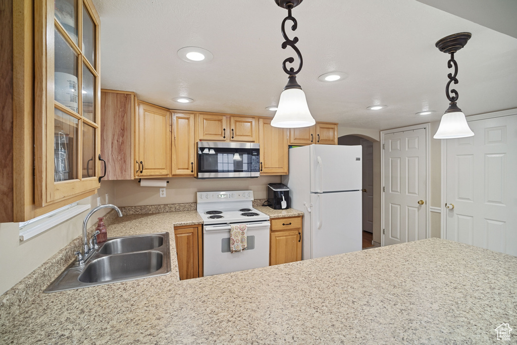 Kitchen featuring white appliances, pendant lighting, sink, and light stone counters