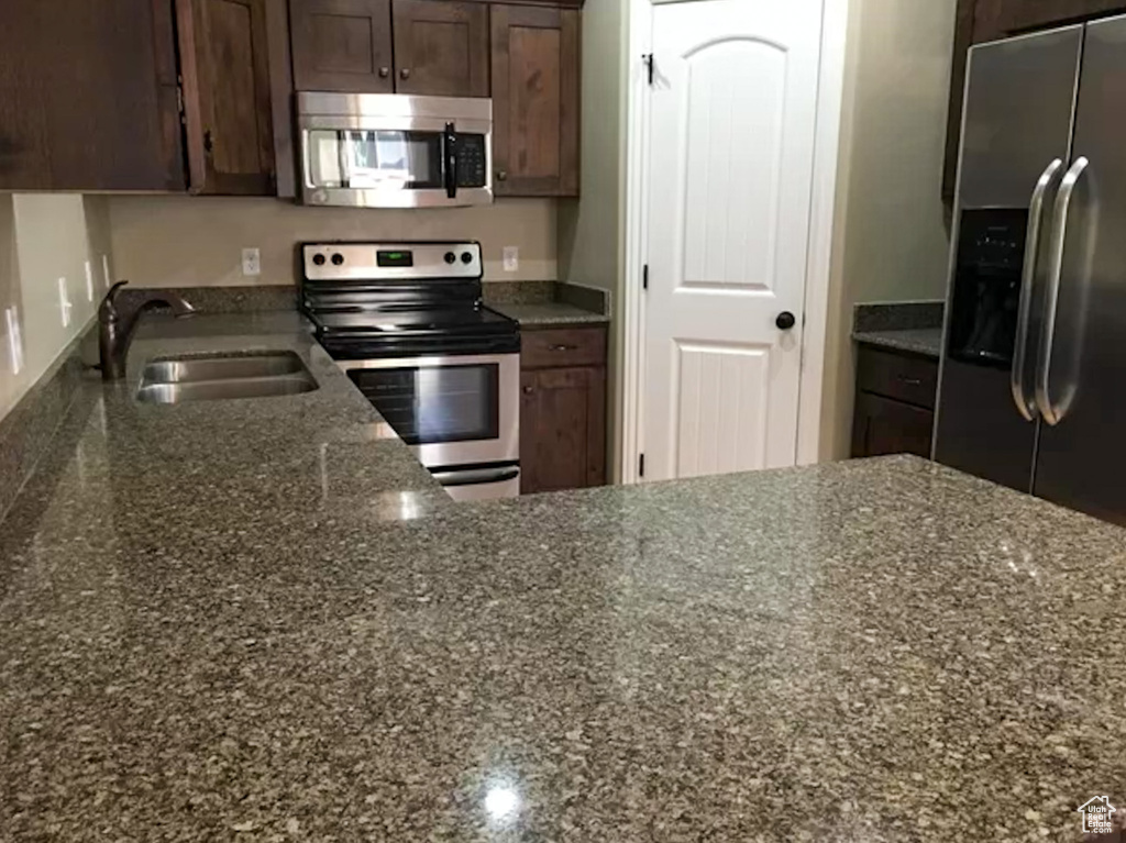 Kitchen featuring appliances with stainless steel finishes, dark brown cabinets, sink, and dark stone counters