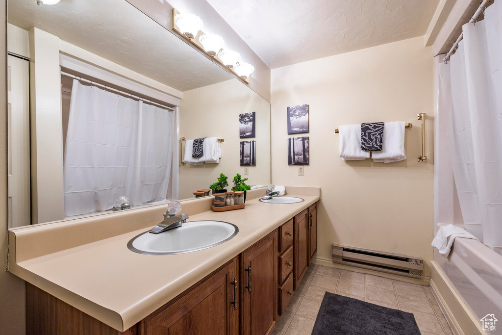 Bathroom with large vanity, double sink, tile floors, a baseboard radiator, and shower / bathtub combination with curtain