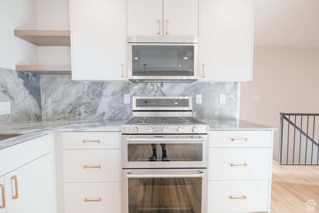 Kitchen featuring tasteful backsplash, stainless steel appliances, light wood-type flooring, and light stone counters