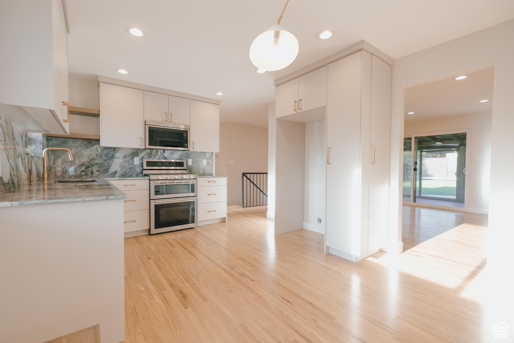 Kitchen with white cabinetry, double oven range, sink, tasteful backsplash, and light hardwood / wood-style floors