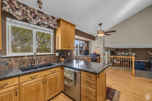 Kitchen with ceiling fan, sink, light hardwood / wood-style floors, stainless steel dishwasher, and dark stone countertops