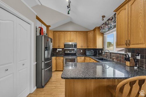 Kitchen featuring appliances with stainless steel finishes, light hardwood / wood-style flooring, lofted ceiling, tasteful backsplash, and sink