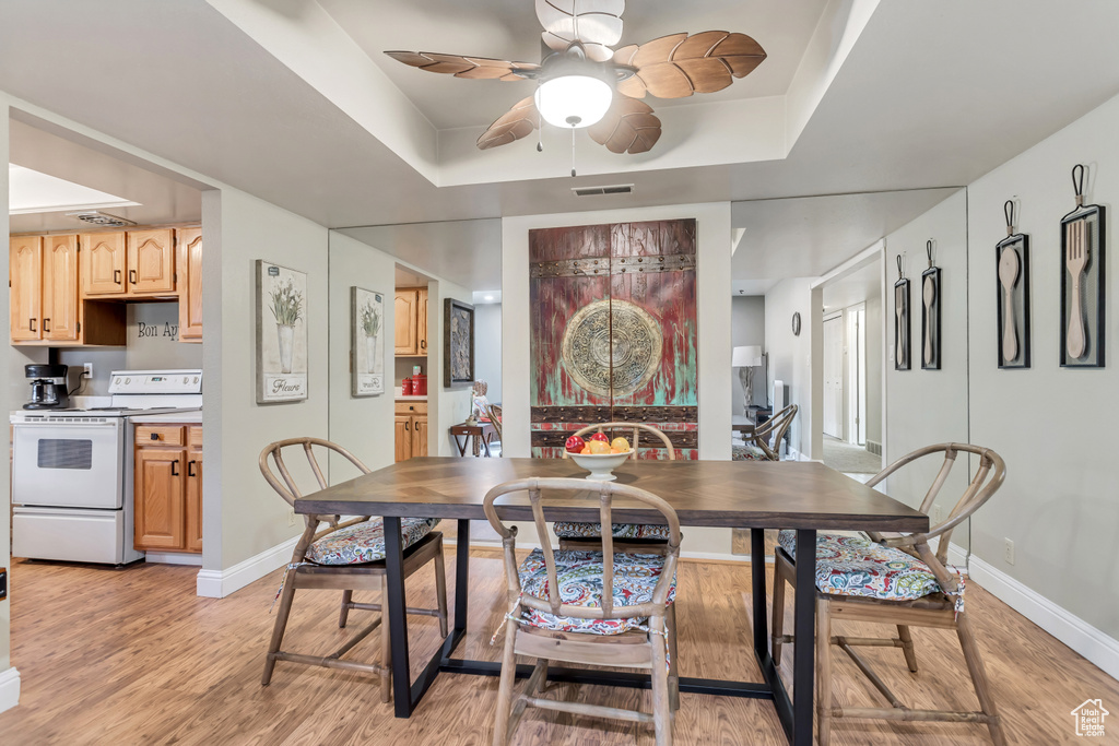Dining room featuring a raised ceiling, ceiling fan, and light hardwood / wood-style floors