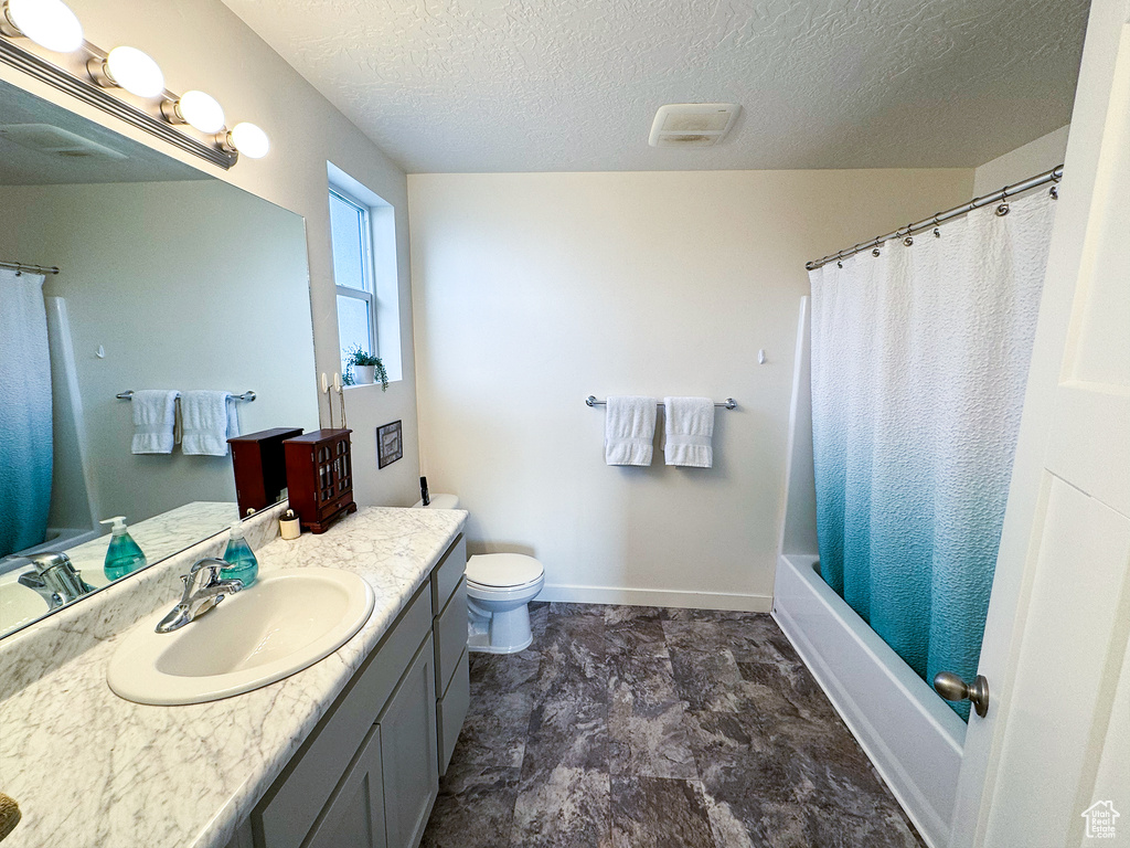 Full bathroom featuring tile flooring, vanity with extensive cabinet space, a textured ceiling, toilet, and shower / bathtub combination with curtain