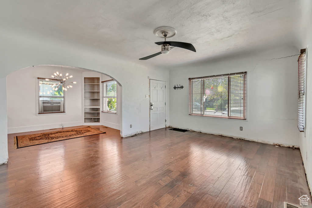 Empty room with built in features, ceiling fan with notable chandelier, and hardwood / wood-style flooring