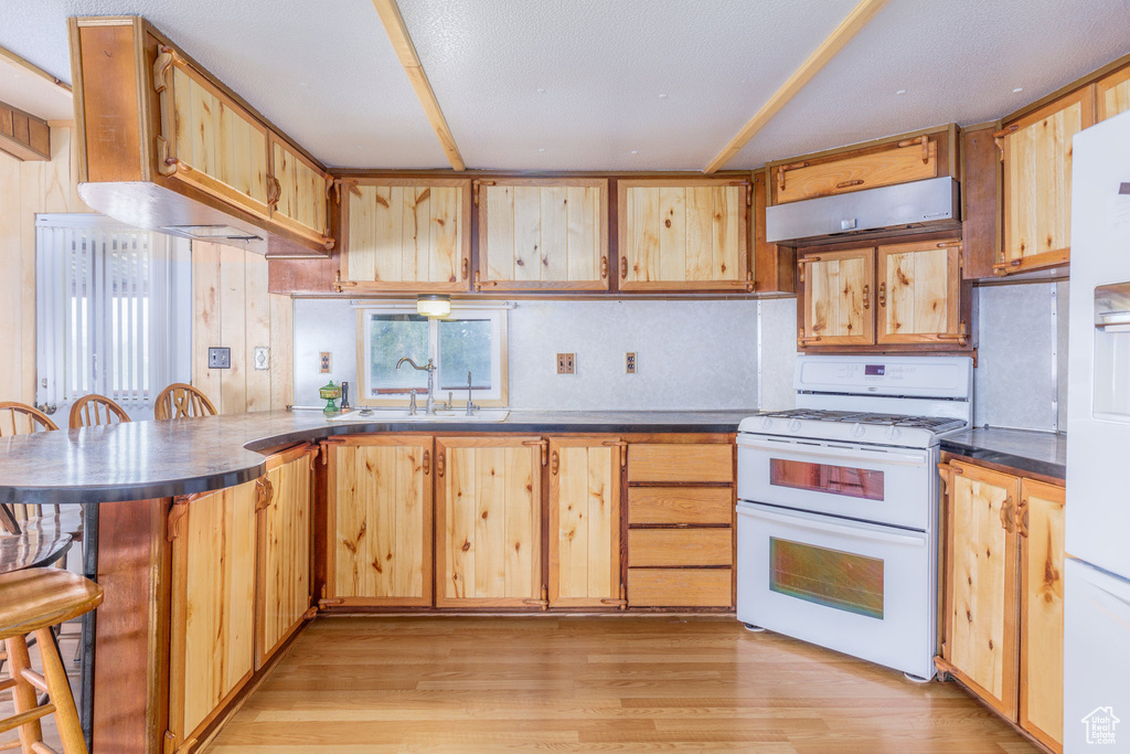Kitchen featuring white range, kitchen peninsula, a kitchen breakfast bar, sink, and light wood-type flooring