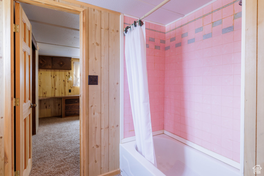 Bathroom with shower / bath combo, wooden walls, and a textured ceiling