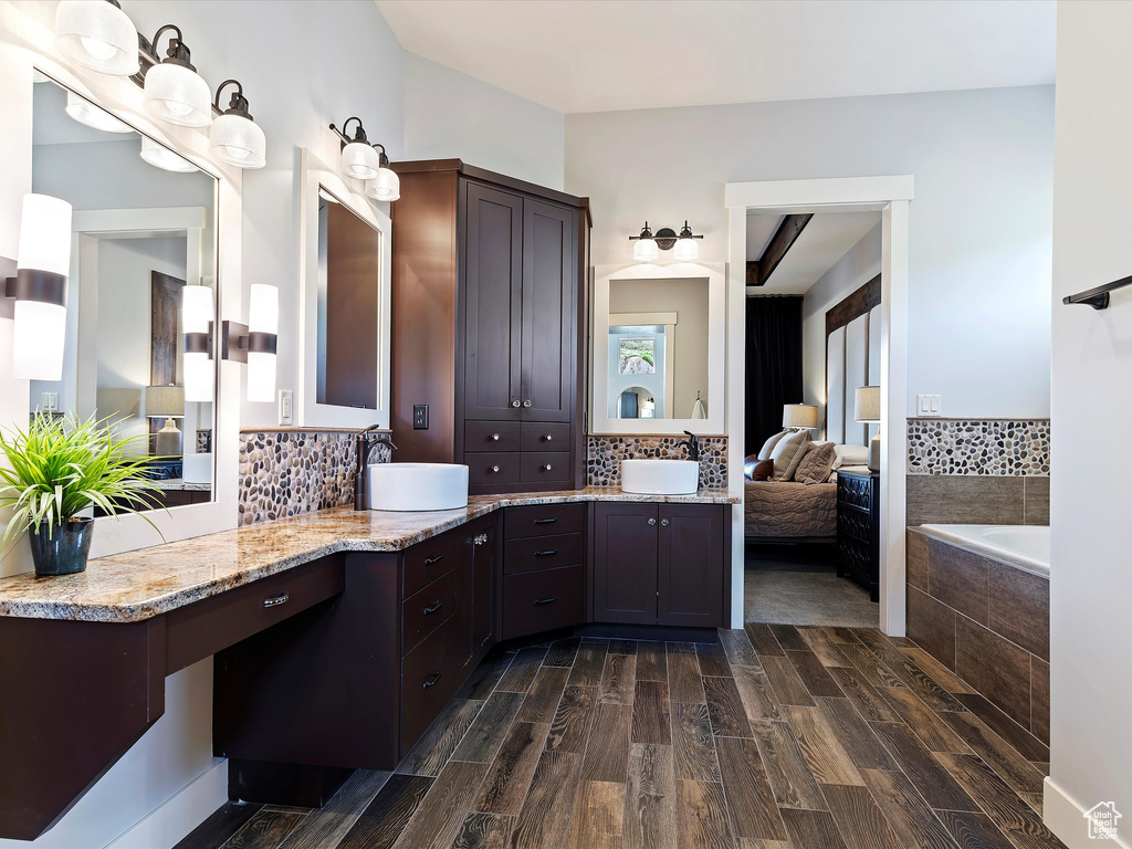 Bathroom featuring backsplash, wood-type flooring, vanity, and tiled tub