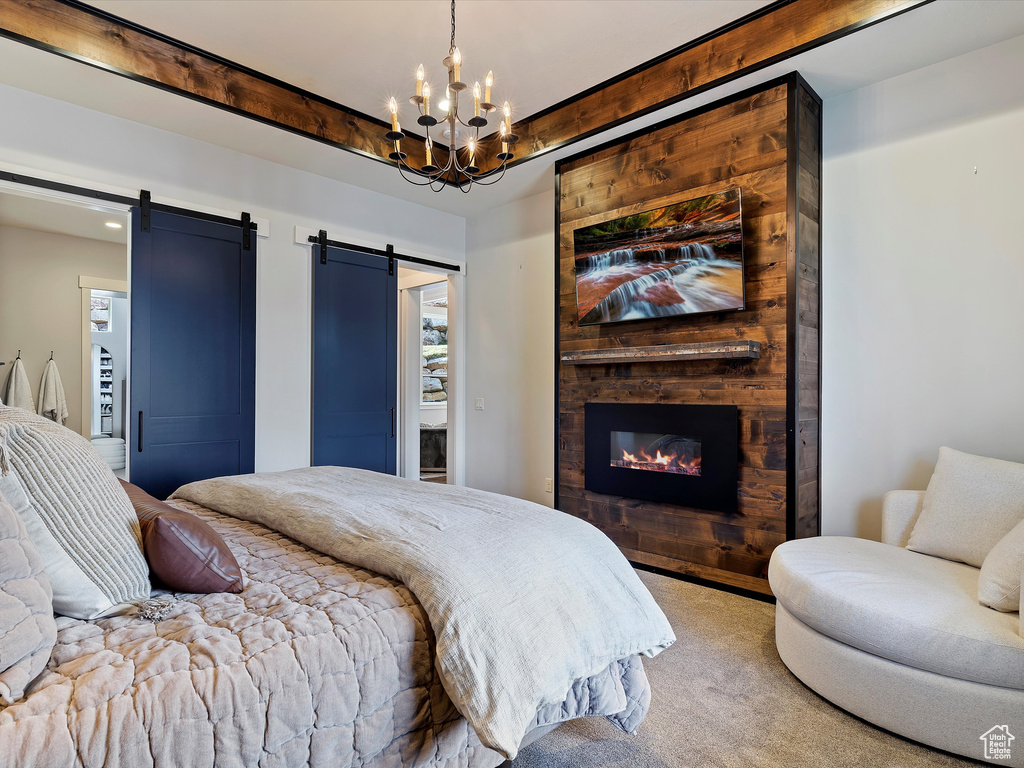 Bedroom with carpet floors, a large fireplace, an inviting chandelier, a barn door, and beam ceiling