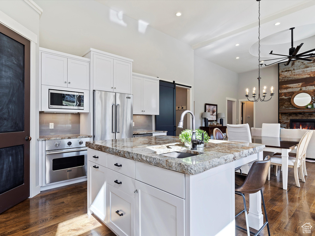 Kitchen featuring backsplash, dark wood-type flooring, stainless steel appliances, and a kitchen island with sink