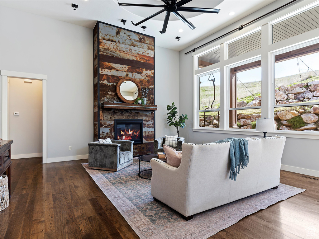 Living room featuring a stone fireplace, dark hardwood / wood-style flooring, and ceiling fan