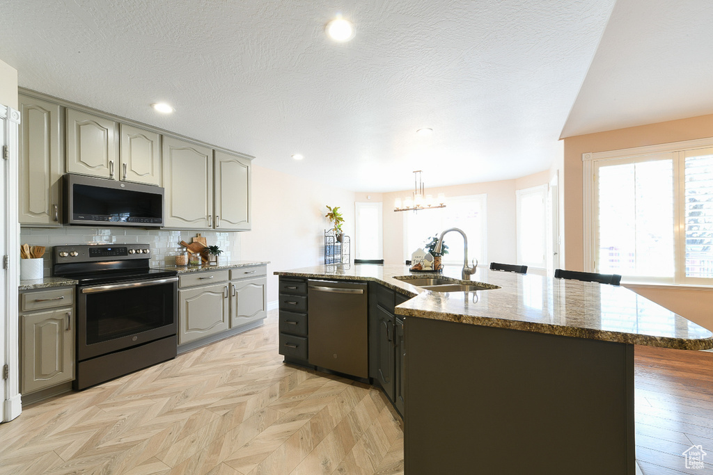 Kitchen featuring appliances with stainless steel finishes, light parquet floors, sink, and a center island with sink