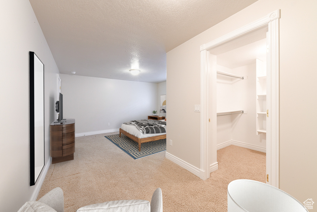 Bedroom featuring light colored carpet, a spacious closet, and a textured ceiling